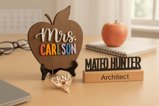 Personalized career gifts display featuring wooden apple nameplate reading Mrs. Carlson for teacher, custom architect desk nameplate reading Mateo Hunter, and gold CRNA medical caduceus pin with gemstone on professional desk with notebook, apple and glass