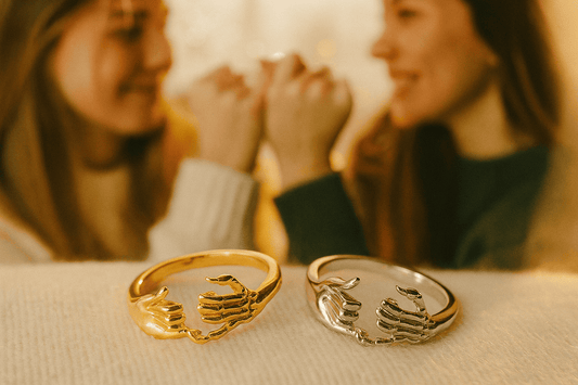 Gold and silver pinky promise rings with hand designs in foreground, two female friends making pinky promise gesture in soft blurred background - personalized friendship gifts